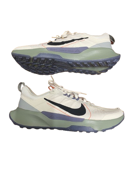 A pair of Nike running shoes shown from the side against a plain white background, featuring a cream mesh upper, a black Swoosh, a muted sage green midsole, and a dark purple outsole.